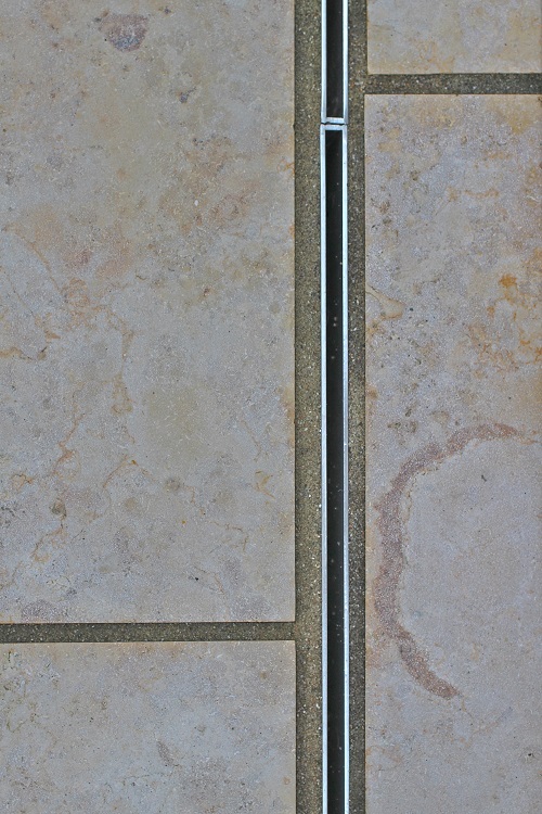 Close-up of stainless steel slot drain set into Jura Beige limestone paving.