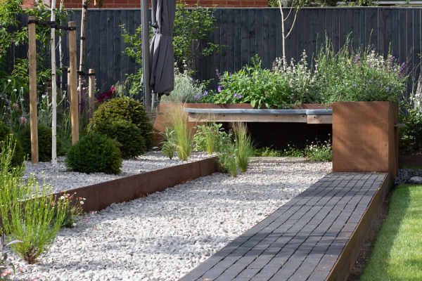 Corten steel planters filled with green and purple plants, a path of amersham clay pavers leads to it with light pebbles on the left.***Adam Vetere Landscape & Garden Design, www.adamvetere.co.uk

