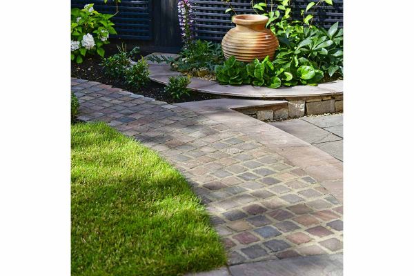 Curved path of Autumn Brown Sandstone Setts with lawn and patio either side, leads to flowerbed and plant pot.***Designed by Painted Fern Garden Design www.paintedfern.co.uk | Built by Sustainable Landscapes Ltd, www.sustainablelandscapes.uk
