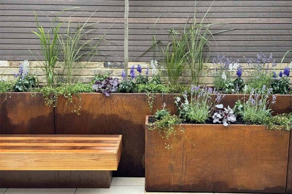 A centred profile of a tall corten steel trough planter featuring green and purple foliage, set against chestnut-toned composite battens.***Chestnut Gardens
