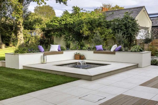 Raised square pond with water feature set in Faro Porcelain patio tiles, with raised beds with matching coping on 2 sides.***Design by Dee Stewart, deestewartgardens.co.uk | Built by Brockstone Landscape Construction Ltd, brockstone.co.uk