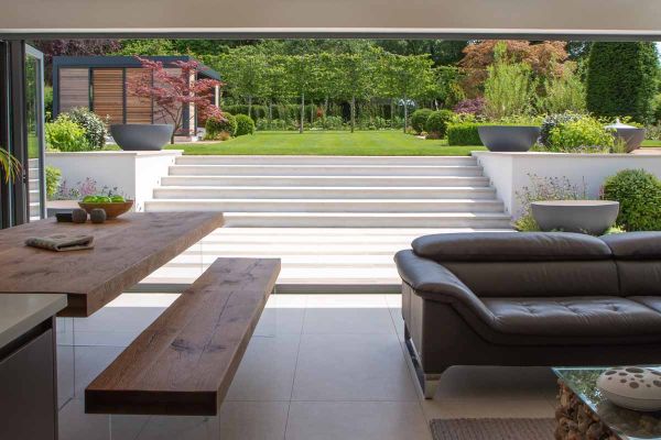 Glorious views of Faro Porcelain Steps with flat wall coping stones from inside, leading up to large lawn area. Design by Caroline Davy.***40mm Downstand | Caroline Davy Studio & PC Landscapes Ltd