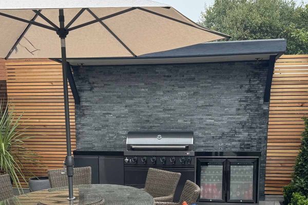 Umbrella seen in foreground, green slate cladding used as splashback and feature wall on outdoor cooking area.***Gordius Team Ltd