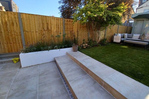2 Cream porcelain outdoor steps rise from patio to lawn between white rendered raised beds. Design by Kingston Landscape Group.***Kingston Landscape Group, www.klguk.com