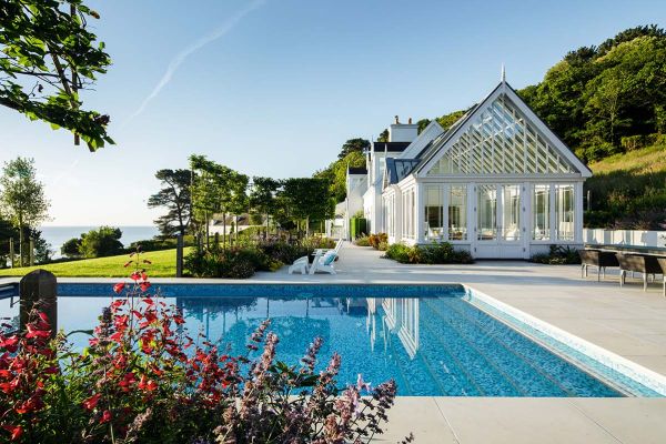 Large swimming pool with Beige smooth sandstone paving surround and view over lawn to the horizon. Design by The Lovely Garden.***The Lovely Garden, www.thelovelygarden.co.uk