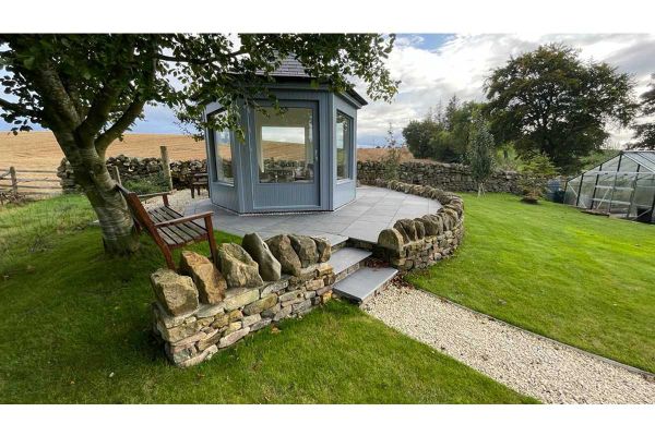 Countryside views enclosed by rock walls show circle patio of midnight black limestone with 3 bullnose steps leading up to small building.***Designed by Twig Garden Design, www.twig-design.co.uk | Built by Faodail Landscapes, www.faodaillandscapes.com