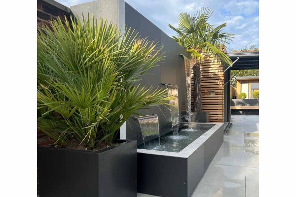 3 tier water feature uses opium black designclad for wall and water trough, palm trees sit either side.***Designed by Shane Matthews | Built by Kent Best Landscapers, www.kentbestlandscapers.co.uk