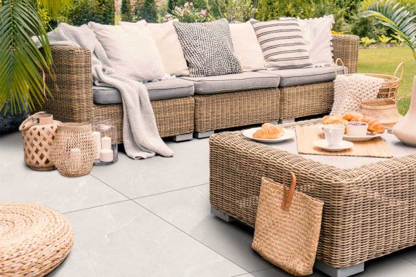 Piazza White porcelain paving in a relaxed garden lounge setting with rattan furniture and neutral-toned decor.***
