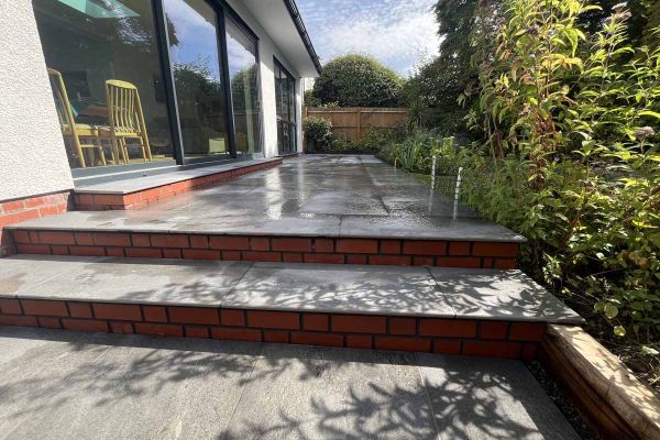 Multi level patio uses platinum grey paving and 20mm bullnose steps against white house with red brick rendered steps.***Vision Garden Design