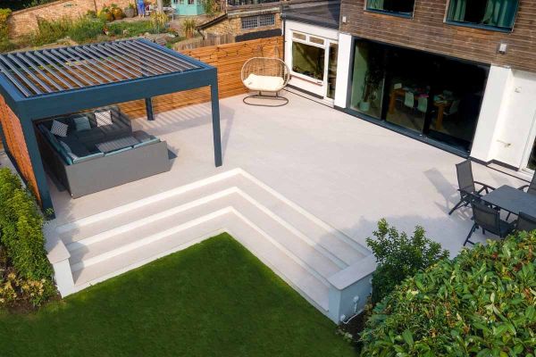 Raised patio with Egyptian Light Porcelain Paving tiles, matching steps, and integrated outdoor seating.***Silvermere Landscapes

