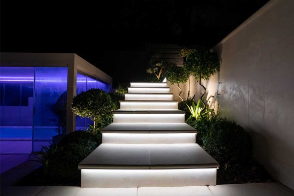 Deep, wide steps with Venetian beige bullnose porcelain treads with underlighting rise between high wall and class building.***36mm Bullnose | Elitescapes