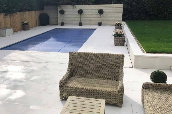 Swimming pool and lounge furniture on porcelain patio with raised flowerbeds capped with comblanchien 40mm downstand copings stones.***Stokes Baldock Ltd