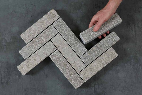 Hand places one Antique Grey limestone brick paver against 9 laid in 3 zigzag rows on dark background. Free UK delivery available.***