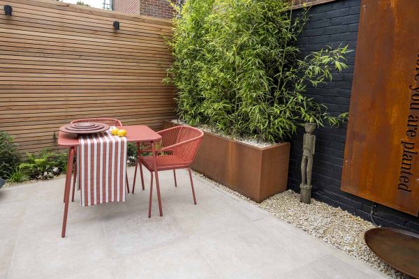 Corten steel panel seen on dark wall as feature, red bistro set sits on egyptian beige limestone patio.***Utopia Landscapes, www.utopialandscapeshp.co.uk
