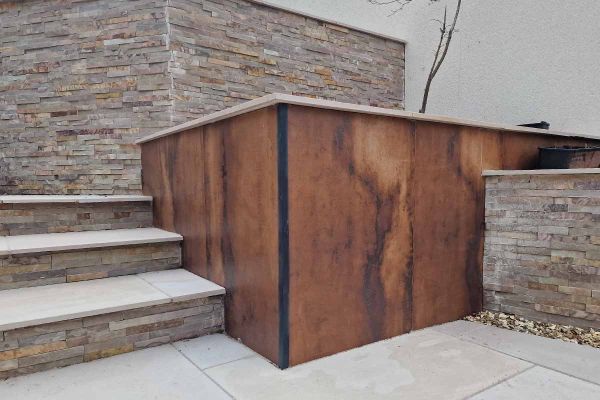 Deep terraced beds, one faced with Siena Copper 1200x600 DesignClad, next to 3 steps with stone-clad risers to match other beds.***Image also displays Burnt Orange Sandstone Cladding | A Star Landscaping, a-star-fencing-landscaping.business.site
