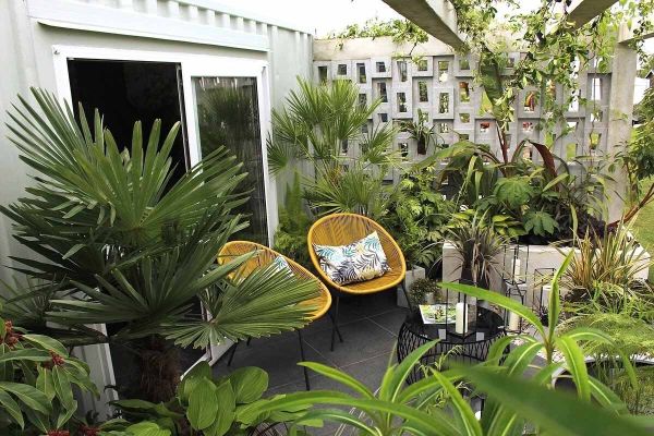 Basalt porcelain seating area with bright yellow chairs and cushions, a round coffee table all surrounded by exotic planting.***Design by Sara Edwards at No.30 Design Studio | Built by Design It Landscapes