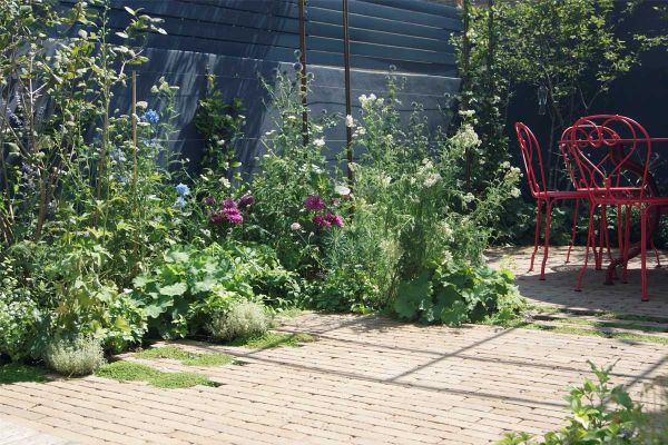 Relaxed planting in irregular-shaped bed between high dark fence and Westminster clay paving with metal furniture.***Designed by Amelia Bouquet Garden Design,  www.ameliabouquetgardendesign.com  |  Built by Urban Meadows,  www.urbanmeadows.co.uk
