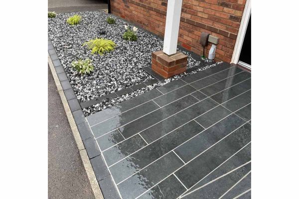 Close-up image of Charcoal Porcelain Planks laid next to area featuring gravel and a few plants, pointed with white grout.***iScape Garden Construction, www.facebook.com/iscapegardens