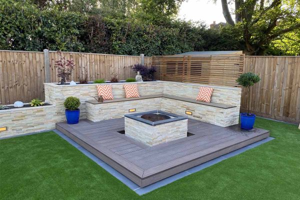 Stone-clad raised bed and bench on 2 sides of deck of Chestnut Grooved decking composite. Firepit in centre with matching cladding.***Gadsden Gardens, www.facebook.com/GGLandscapers