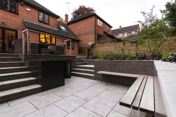 Two sets of steps descend from suburban house to silver-grey porcelain patio, enclosed by raised beds. Design by Creative Roots.***Creative Roots, www.creativeroots.com