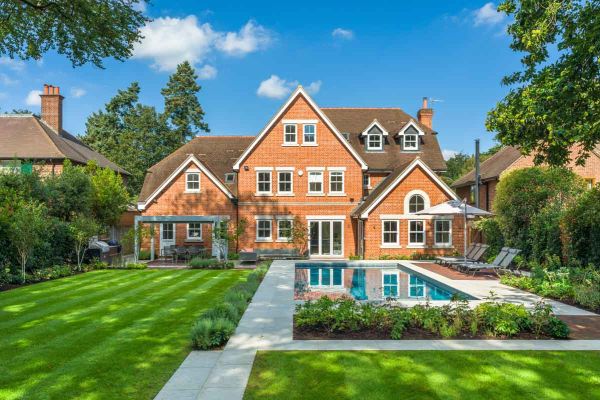 Dove Grey Sawn Sandstone paving surrounds blue-lined swimming pool, separating it from lawn, at back of large gabled house.***Graduate Landscapes,  www.graduatelandscapes.co.uk