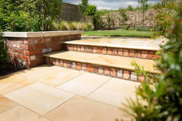Paving slabs in front of 2 Dune Smooth Sandstone Bullnose steps, with brick risers and piers, rise to lawn surrounded by beds.***Barnes Walker,  www.barneswalker.co.uk