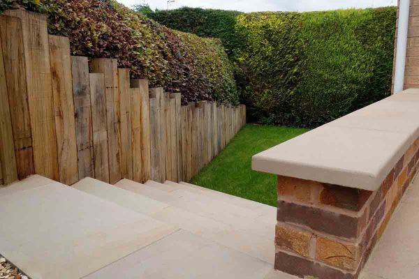 Steps descend between fence of upright wooden sleepers and low parapet topped with Buff swimming pool coping stones.***Elizabeth Buckley Garden Design