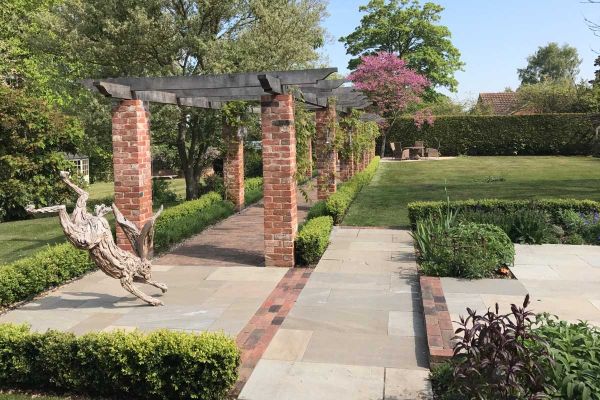 Wooden hare sculpture on paving with Romsey Antique clay bricks detailing at end of colonnade of brick pillars next to lawn.***Roger Gladwell Landscape & Construction Ltd, www.rogergladwell.co.uk
