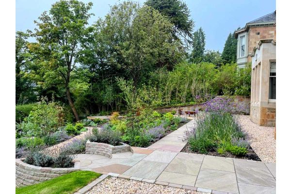 2 curved raised beds of Raj Green sandstone walling embrace paving circle on terrace descending from back of stone-built house. ***Designed by Glen Rosa Garden Design, www.glenrosagardendesign.co.uk | Built by Faodail Landscapes, www.faodaillandscapes.com