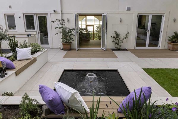 Fountain in midst of square pond with edges recessed beneath Faro porcelain coping with 40mm downstand, part of patio of house.***Designed by Dee Stewart Garden Design, www.deestewartgardens.co.uk | Built by Brockstone Landscape Construction Ltd, www.broc