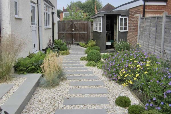 Sinuous path of Flamed Grey Smooth Sandstone paving slabs set into gravel runs between house and flower beds to tall wooden gates.***Designed By Helen Rose Wilson Garden Design,  www.helenrosewilson.com | Built by DW Outdoor Living,  www.dwoutdoorliving.c