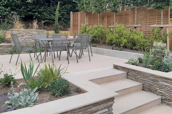 Steps with flowerbeds either side lead up to patio are with dining table using florence beige porcelain paving.***Anna Helps Garden Design, www.annahelpsgardendesign.co.uk
