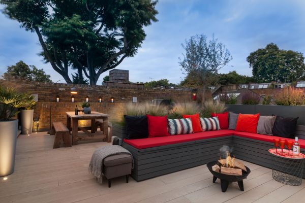 Small firepit burns in centre of corner bench on golden oak millboard decking surrounded by brick walls and garden lighting.***Georgia Lindsay Garden Design, www.georgialindsaygardendesign.co.uk

