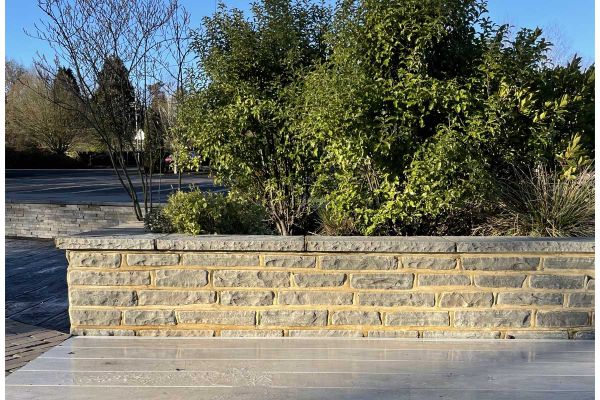 Low block of grey sandstone garden walling, capped with coping. Large shrub stands on other side. Free UK delivery available.***Kent Showroom @ London Stone
