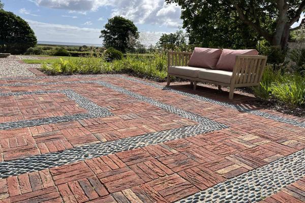 2-seater outdoor sofa at edge of rectilinear area paved with Old English Belgian bricks laid basketweave with pebble detailing.***Hal Forbes Adam, www.halforbesadam.com
