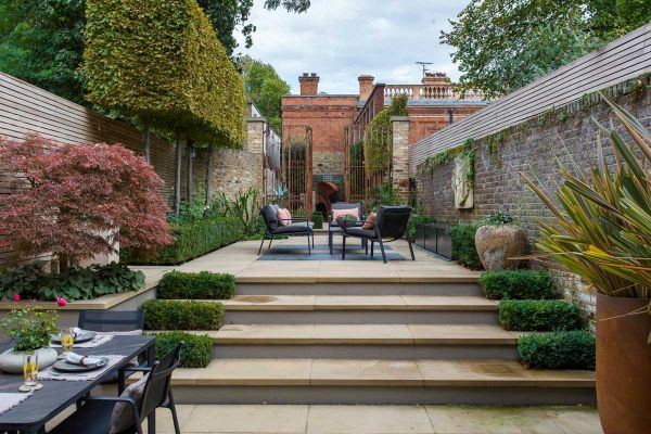 Britannia Buff Yorkstone bullnose steps rise to narrow, paved walled garden with tall metal gates at end and beds down each side.***Harrington Porter, www.harringtonporter.com