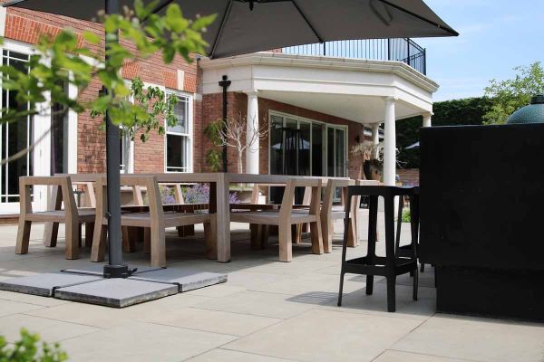 Heath smooth sandstone patio paving at rear of brick house with 5 sided balcony. Cantilevered parasol shelters dining set.***Living Landscapes,  www.livinglandscapesuk.com
