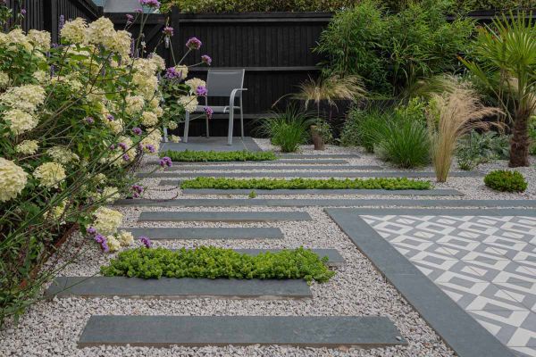 Close-up image of Charcoal Porcelain Planks laid next to area featuring gravel and a few plants, pointed with white grout.***iScape Garden Construction, www.facebook.com/iscapegardens