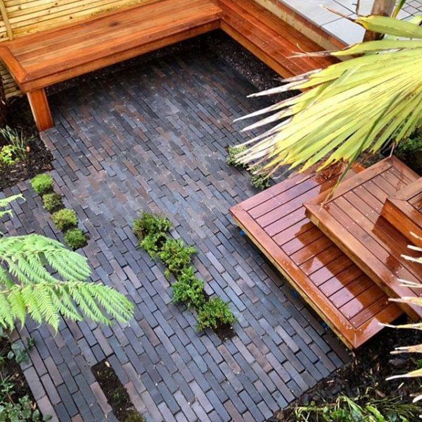 View down to 3 intersecting square wooden steps descending to small area  paved with Ancona Dutch clay pavers, with inbuilt bench.***Designed by Osmosis Garden Design, osmosisgardendesign.co.uk | Built by Royal Gardens, www.royal-gardens.co.uk
