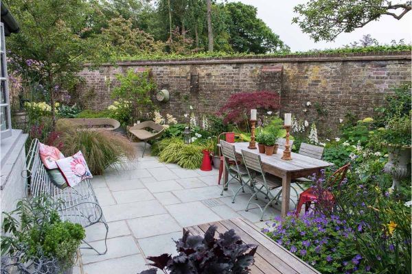 Kota Blue limestone garden patio laid with project paving, bounded by tall, old brick wall and colourful flower bed.***Nic Howard, We Love Plants,  www.we-love-plants.co.uk
