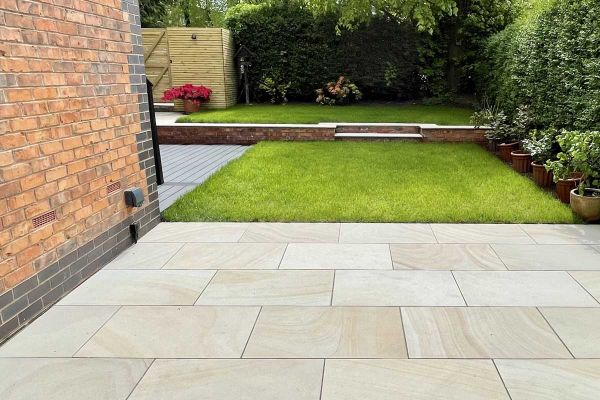 Light Buff sawn sandstone 900x600mm paving adjacent to rectangular lawn with steps up to second grass area beyond.***Bark, Brick & Block, www.barkbrickblock.com