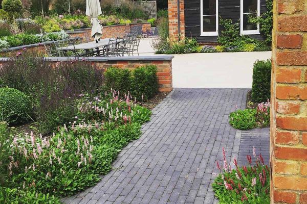 Path of Lucca Dutch clay pavers runs past planted border to L-shaped white patio wrapped around corner of house.***Designed by Andrea Newill Garden Design, www.andreanewill.co.uk | Built by Simply Green Landscapes, www.simplygreenlandscapes.co.uk
