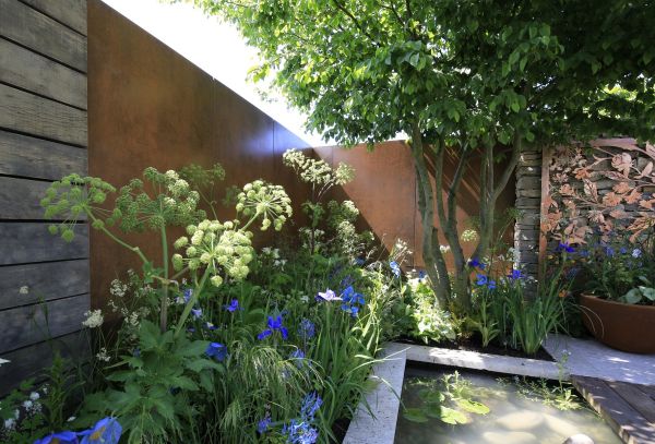 Sun pokes through steel corten luxury designclad clad between fencing, onto heaving flowerbed next to tree and pond.***Designed by David Neale | Built by Neale Richards Garden Design
