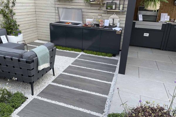 Wood effect paving slabs laid in a path towards an outdoor kitchen with seating area and timber screen background.***Garden House Design,  www.gardenhousedesign.co.uk