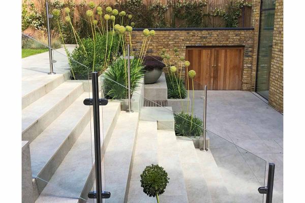 Silver Grey Porcelain Garden Steps descending on to patio, glass panels used as railings with green Alliums planted up the stairs in built in beds.***James Lee Landscape & Garden Design, www.jamesleedesign.com

