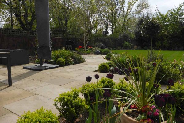 Raj Green Indian Sandstone patio paving runs through planting beds and out onto large lawn in fenced in garden.***Landscape Artisan, www.landscapeartisan.co.uk | Janice Cripps, www.janicecripps.co.uk
