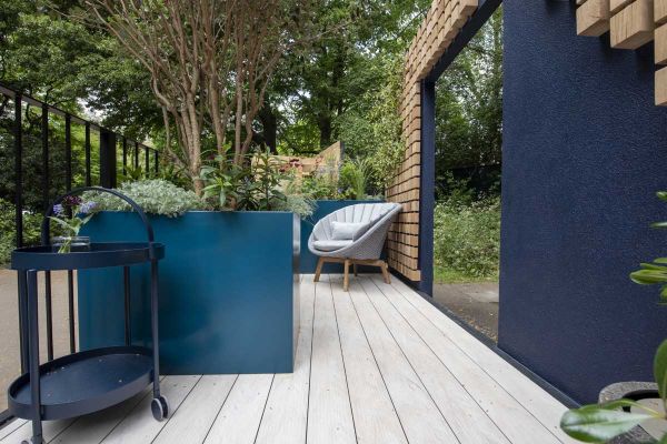 Large planters on Polar DesignBoard composite decking, between railings and blue wall in The Reading Room garden, RHS Chelsea 2023.***Designed by Katherine Holland, www.katherine-holland.co.uk | Built by Phil Sutton Landscapes, www.instagram.com/philsutto