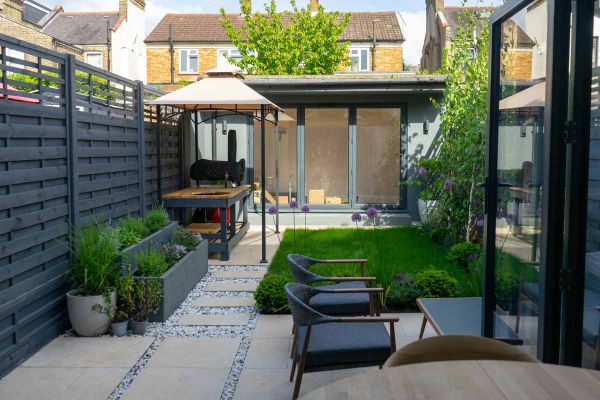 Path of Jura Beige porcelain outdoor tiles UK set into gravel leads from patio area to garden studio past a covered work bench.***Imago Gardens Ltd, www.imagogardens.co.uk
