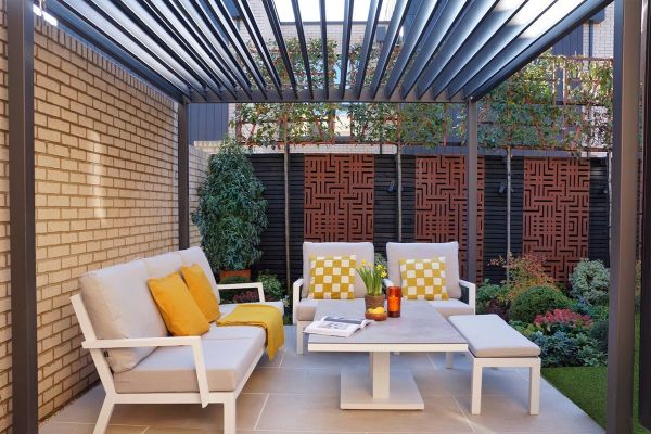 Proteus Grey weatherproof pergola with roof louvres open, sits over lounge set on patio next to house wall.***East London Garden Design, www.eastlondongarden.com