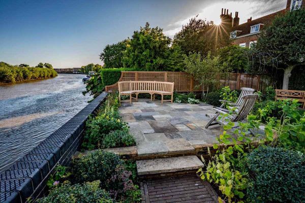 Riverside patio of reclaimed Yorkstone paving with wooden seating, shrubs and trellis fence. 2 steps down to clay paver path.***Shoots & Leaves, www.shootsandleaves.co.uk
